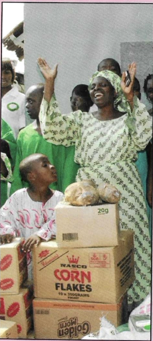 A beneficiary raising her hands in gratitude beside donated supplies